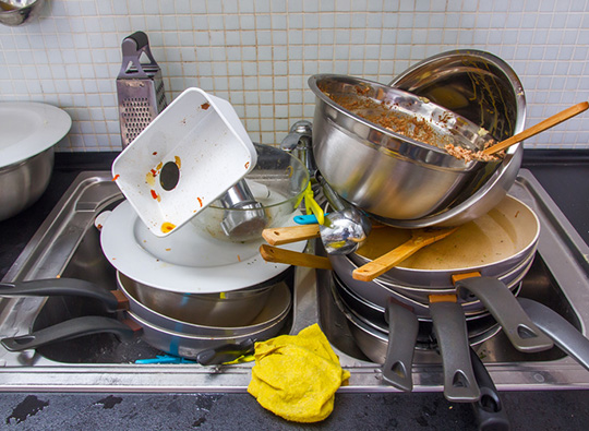 An image of unwashed crockery and pans piled in a sink.