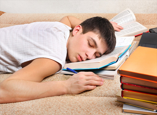 An image of a young man who has fallen asleep on an open book.