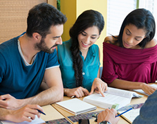 An image of three people looking at a book together.